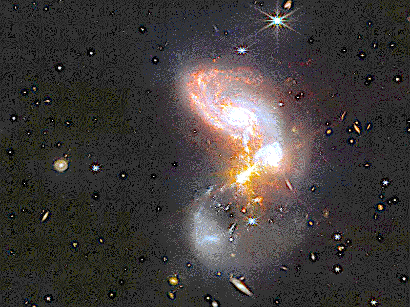 A merging galaxy pair cavort in this image captured by the NASA/ESA/CSA James Webb Space Telescope. This pair of galaxies, known to astronomers as II ZW 96, is roughly 500 million light-years from Earth and lies in the constellation Delphinus, close to the celestial equator. As well as the wild swirl of the merging galaxies, a menagerie of background galaxies are dotted throughout the image.The two galaxies are in the process of merging and as a result have a chaotic, disturbed shape. The bright cores of the two galaxies are connected by bright tendrils of star-forming regions, and the spiral arms of the lower galaxy have been twisted out of shape by the gravitational perturbation of the galaxy merger. It is these star-forming regions that made II ZW 96 such a tempting target for Webb.